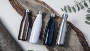 A variety of vibrant stainless steel water bottles with different shapes and colors, placed against a minimalistic, eco-friendly background with green leaves.